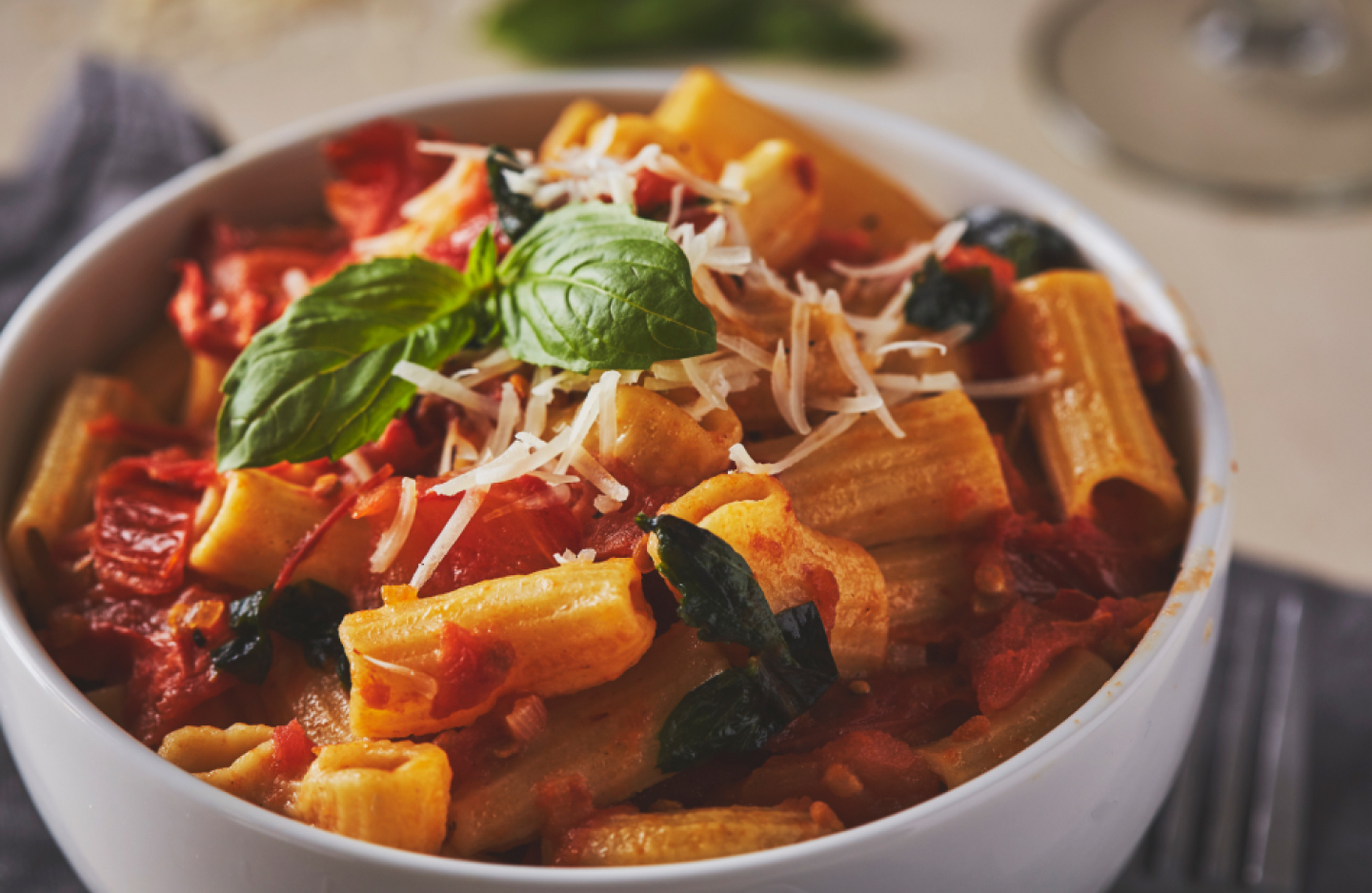 A bowl of rigatoni pasta with fresh tomato sauce, basil and cheese
