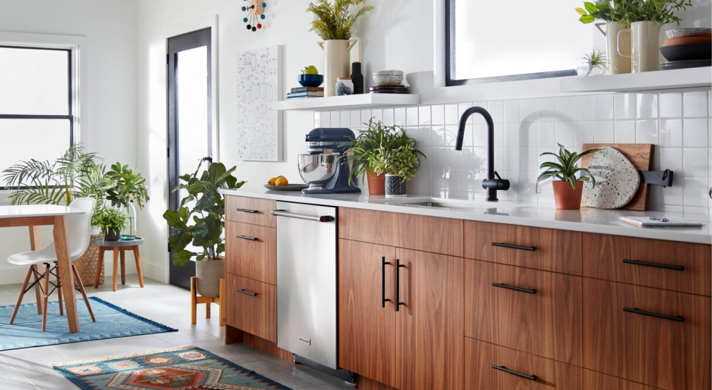 Blue KitchenAid® Artisan stand mixer sitting on white countertop in white modern kitchen with open shelving and brown wooden cabinets.