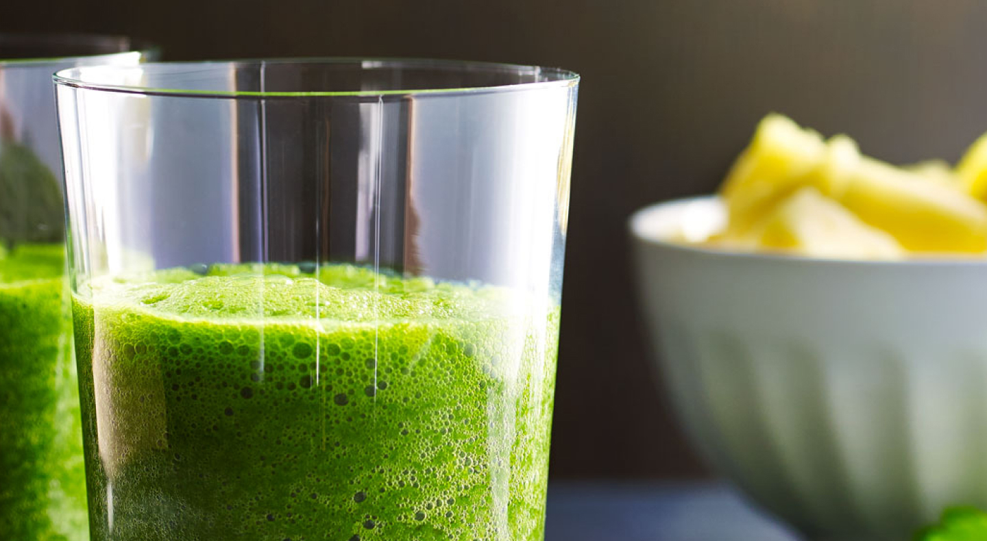 A bowl of fruit next to a glass of kale juice