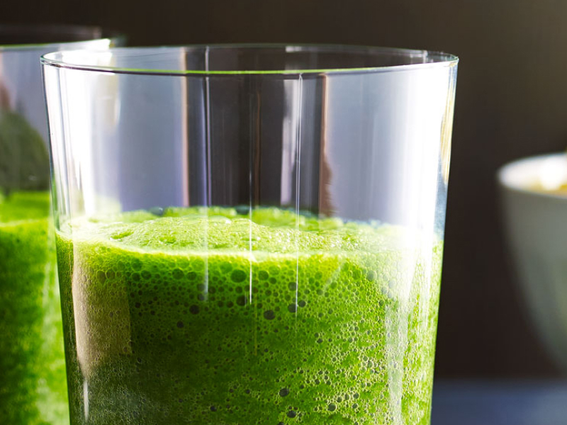 A bowl of fruit next to a glass of kale juice