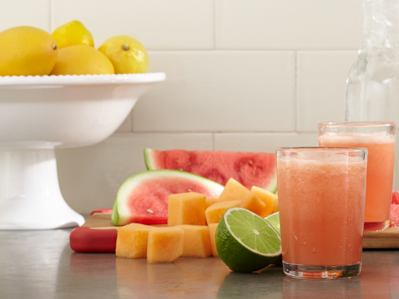 Glasses of fresh juice next to assorted fruit pieces