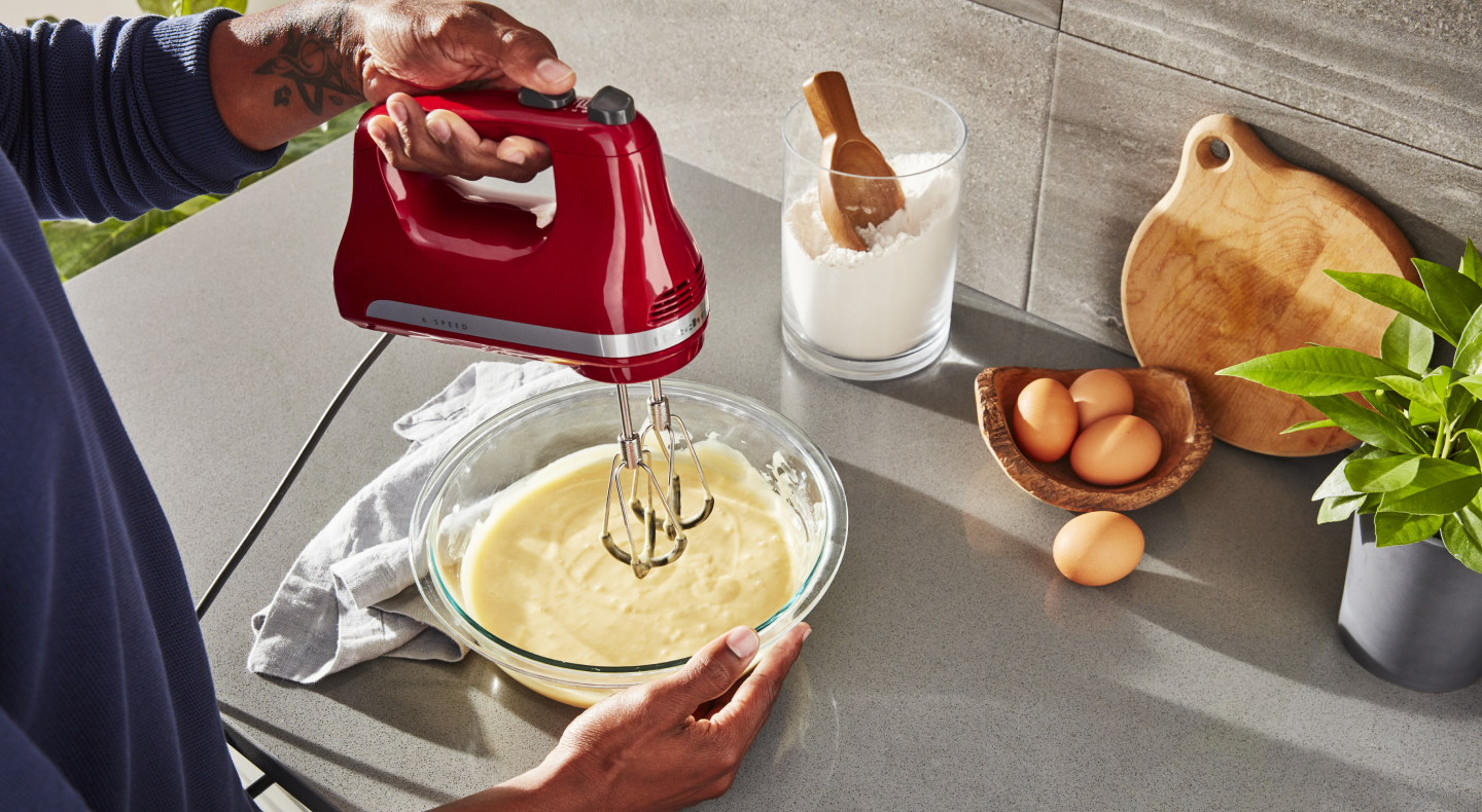 Person using KitchenAid® hand mixer over bowl of batter
