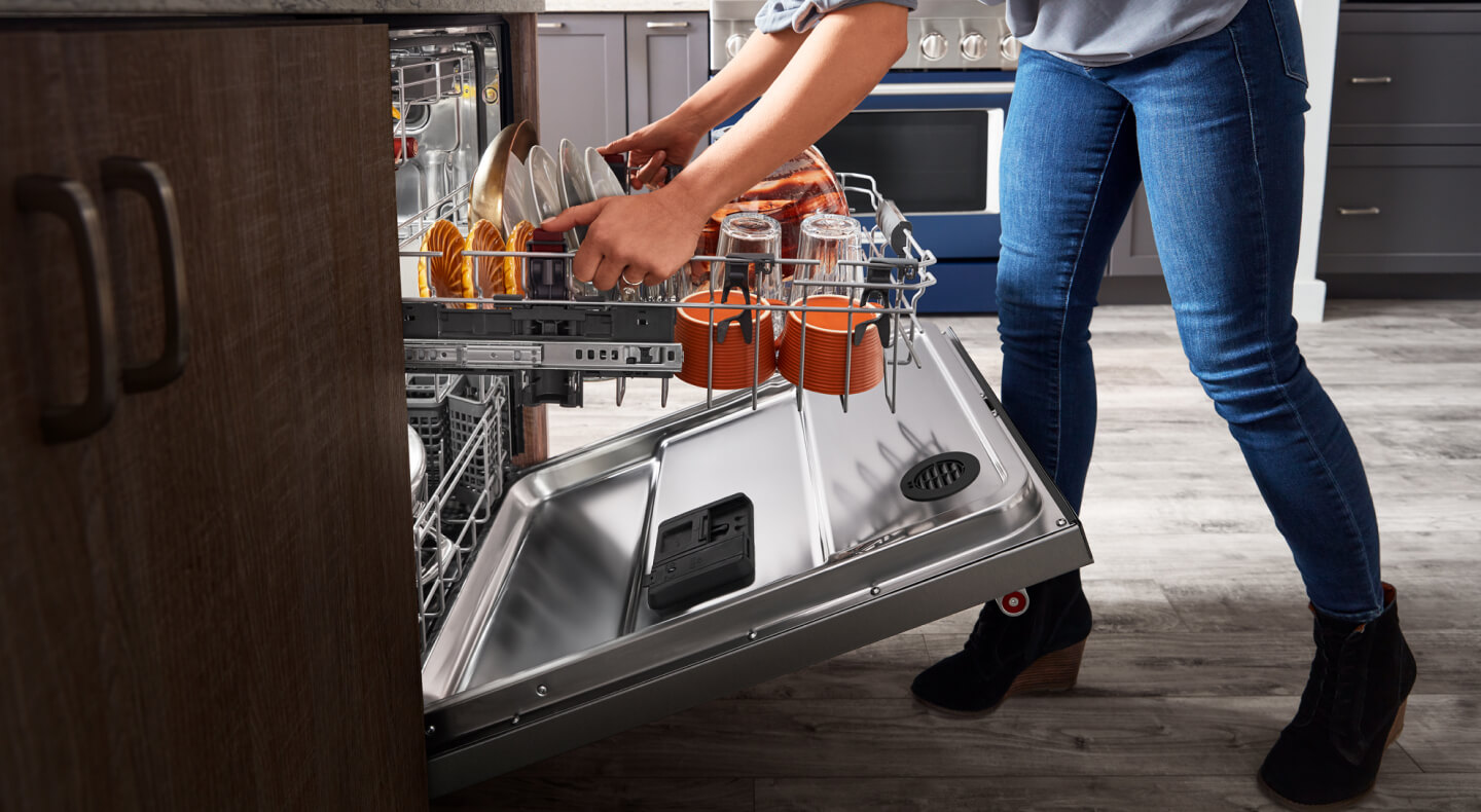 Person adjusting upper rack height of a loaded dishwasher with a third rack