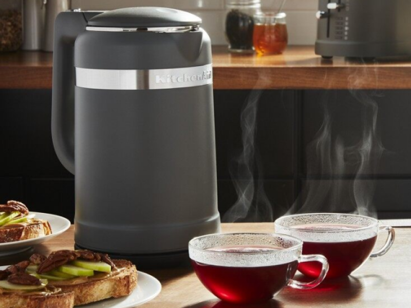 Electric tea kettle on a kitchen island next to cups of tea and toast.