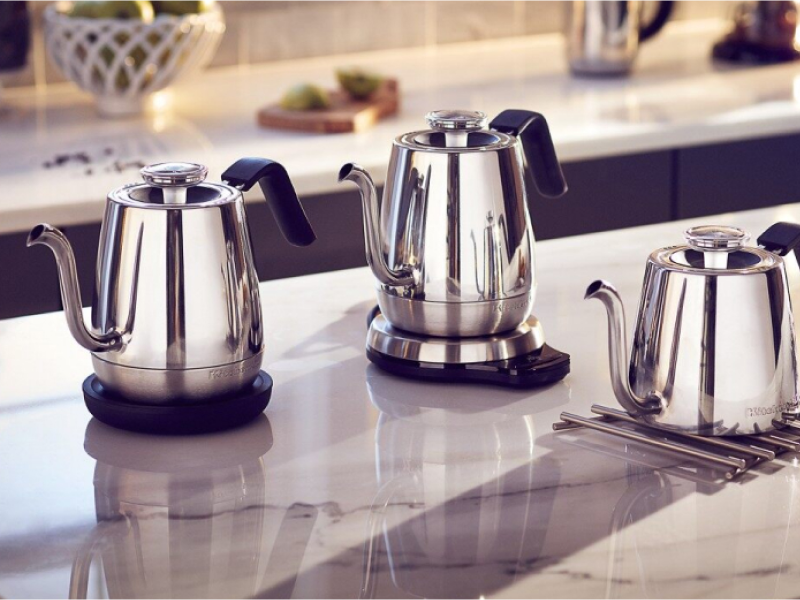 Three KitchenAid® electric tea kettles on the island next to cups of tea and cookie tray.