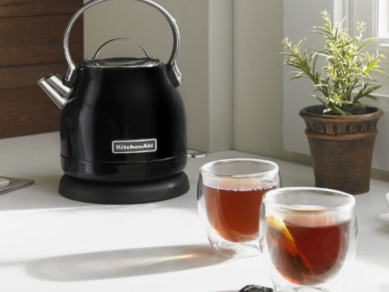 Black KitchenAid® 1.25 L Electric Kettle on a counter next to full cups of tea.