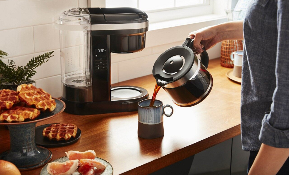 Person pouring coffee into a mug with coffee maker in background