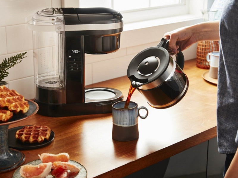 Person pouring coffee into a mug with coffee maker in background