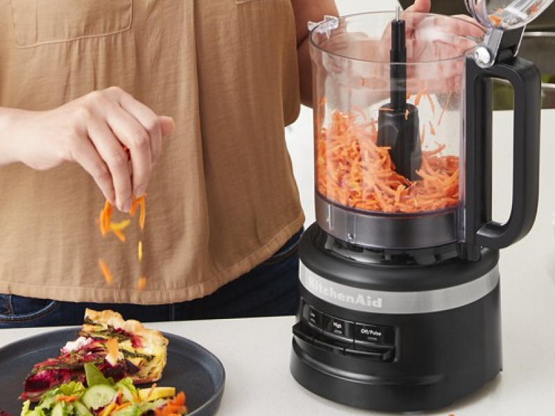 Person shredding carrots in a black food processor