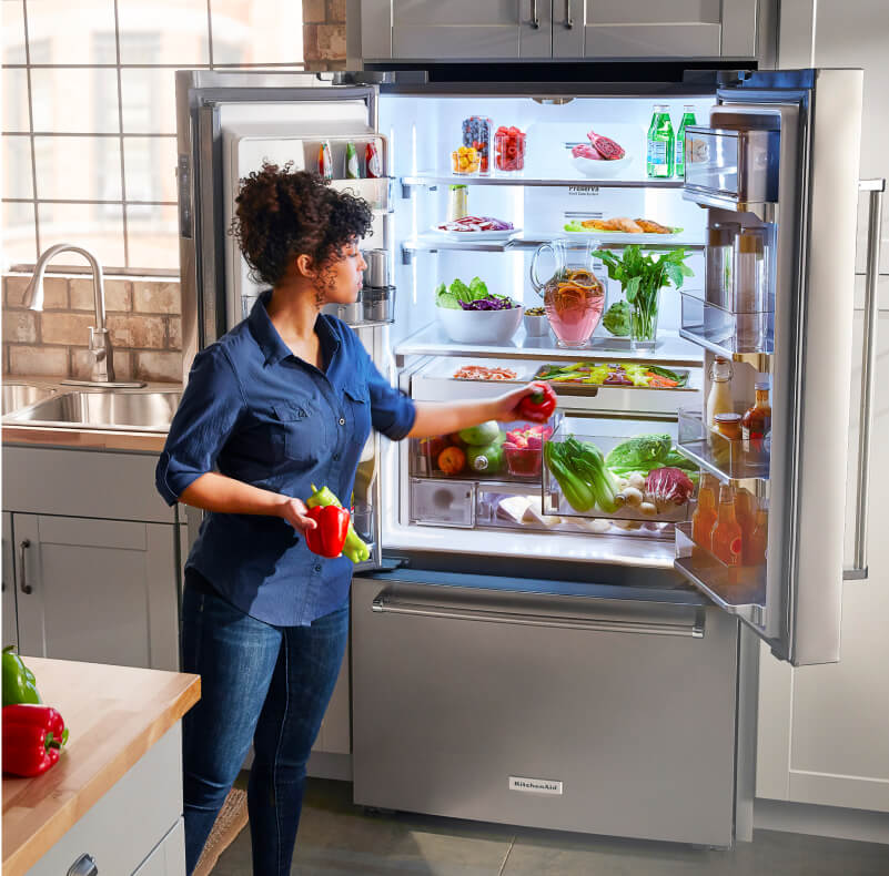 A person placing red and green peppers in a crisper drawer