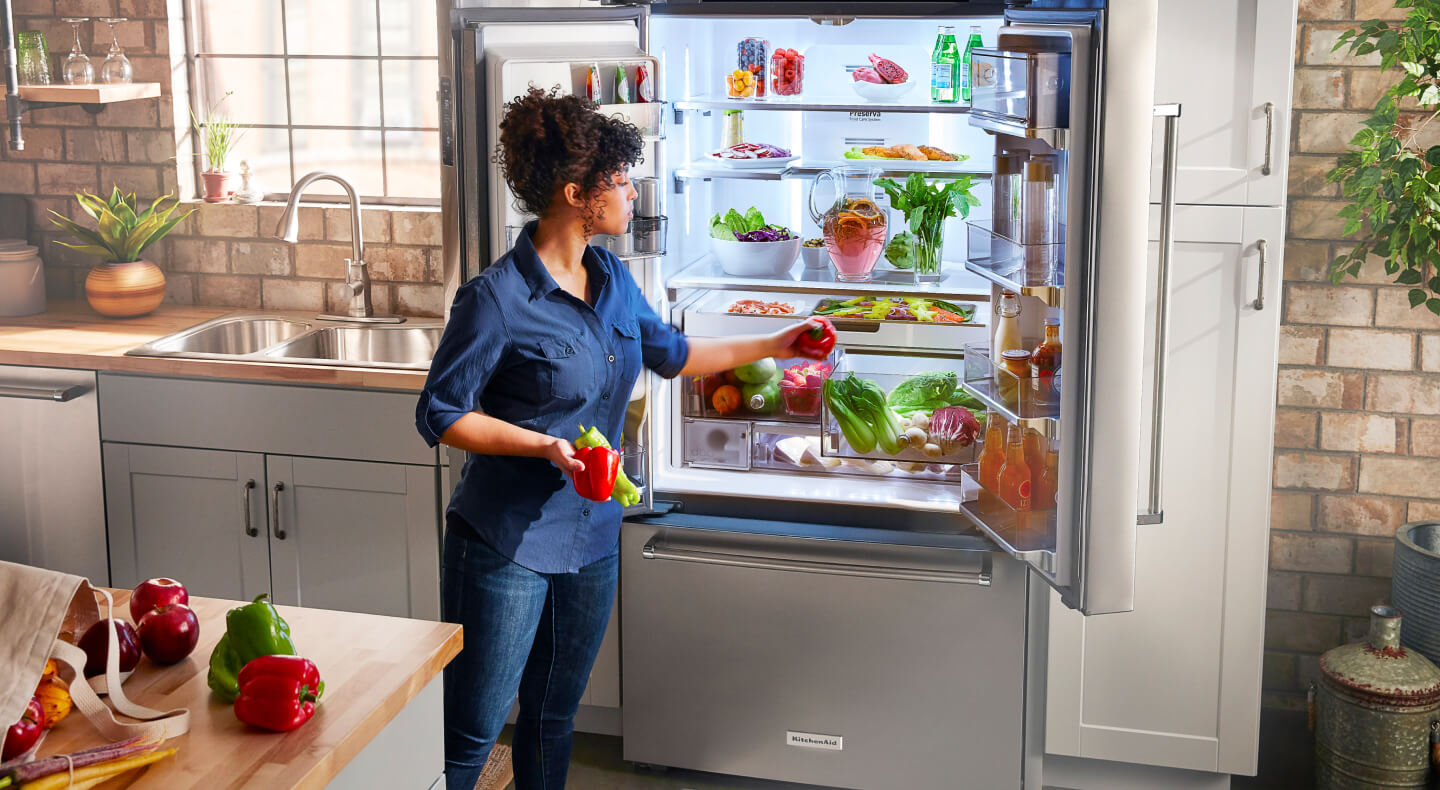 A person placing red and green peppers in a crisper drawer