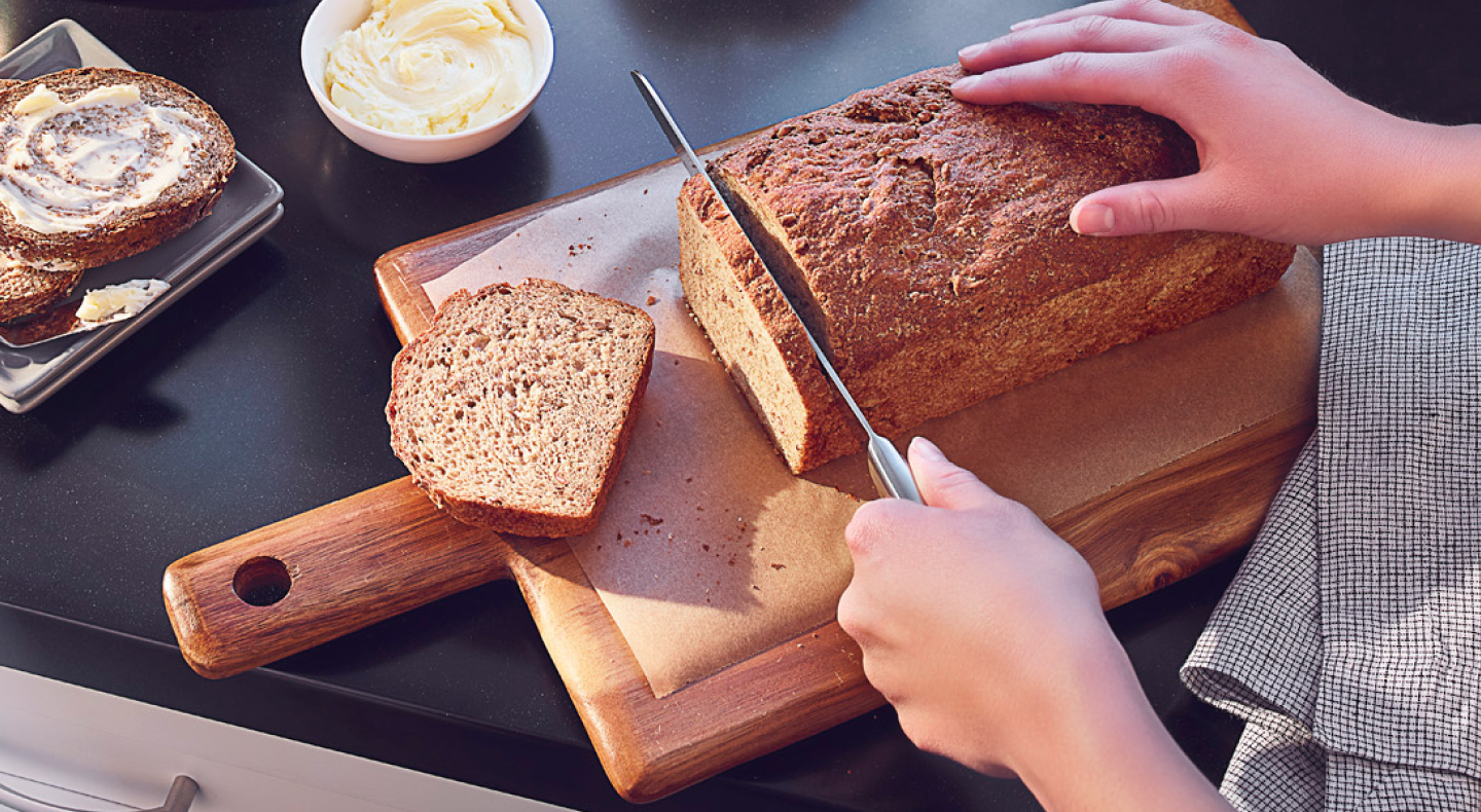 Person slicing a loaf of bread on a wooden cutting board