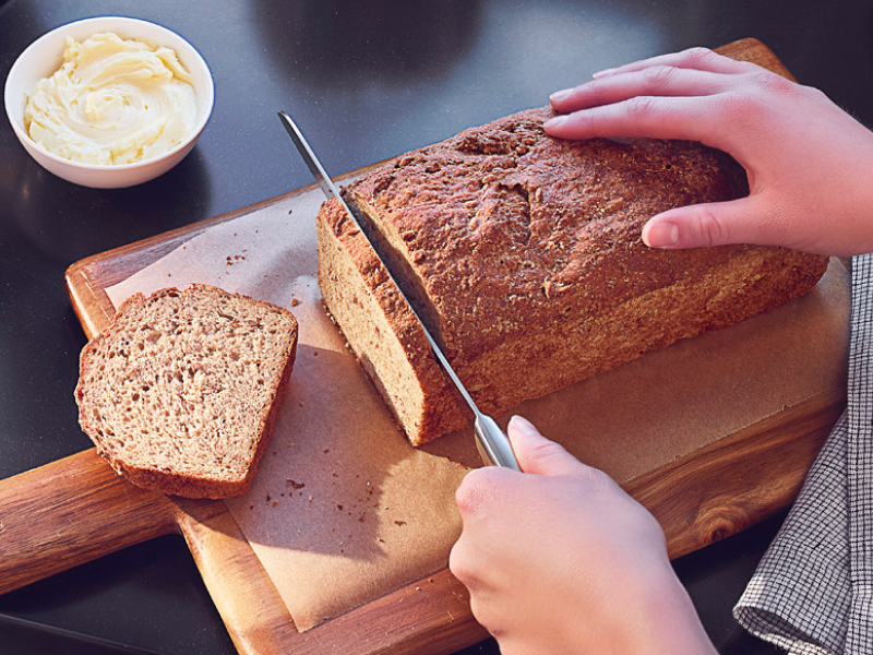 Person slicing a loaf of bread on a wooden cutting board