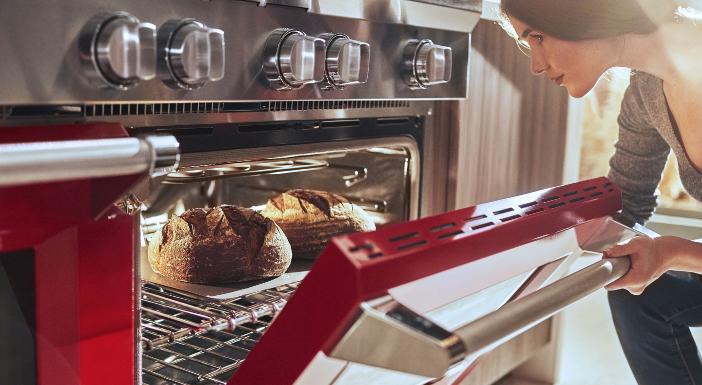 A woman pulling freshly baked bread out of an oven