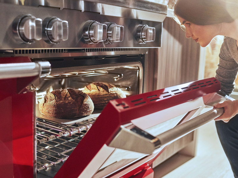 A woman pulling freshly baked bread out of an oven
