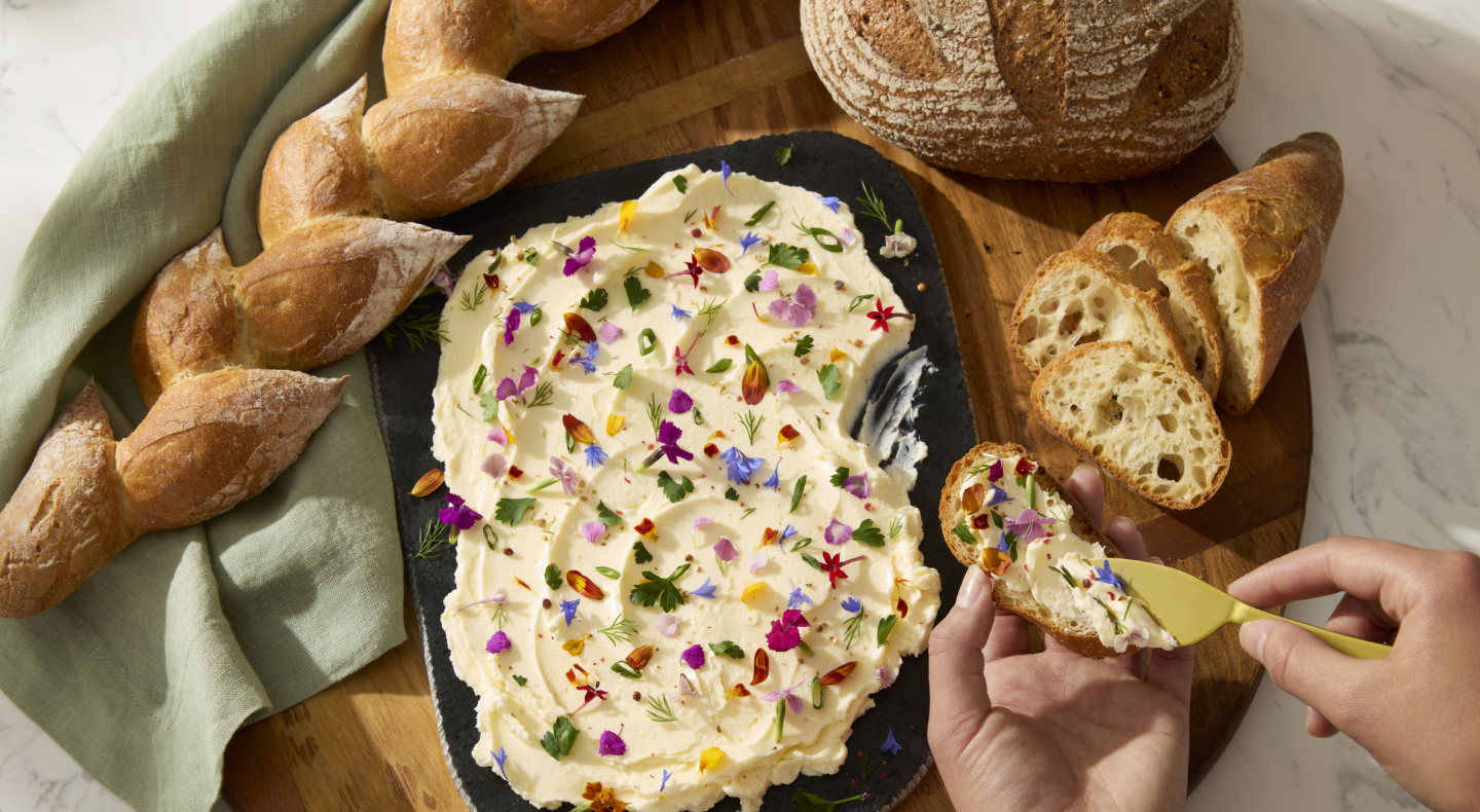 A person topping a loaf of baked bread with a homemade spread