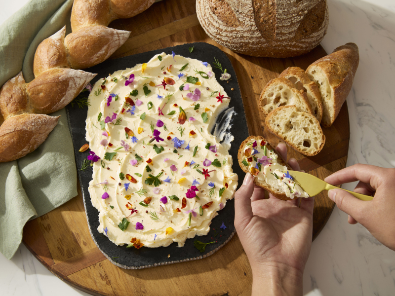 A person topping a loaf of baked bread with a homemade spread