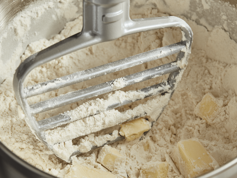 Paddle attachment cutting butter into flour in a mixing bowl 