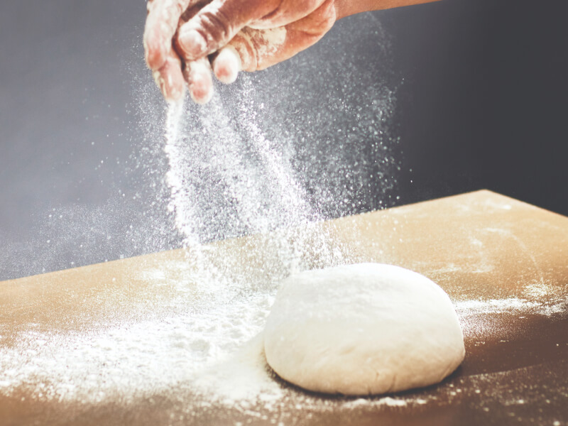 Person sprinkling flour over a ball of dough