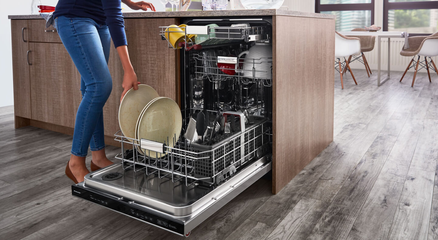 A woman placing a plate in a dishwasher