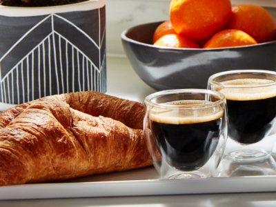 Croissants and cups of espresso on a tray in front of a bowl of oranges.