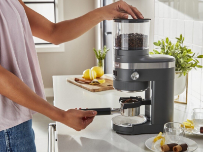 Hand placing portafilter under burr coffee grinder.