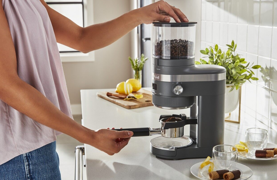 Hand placing portafilter under burr coffee grinder.