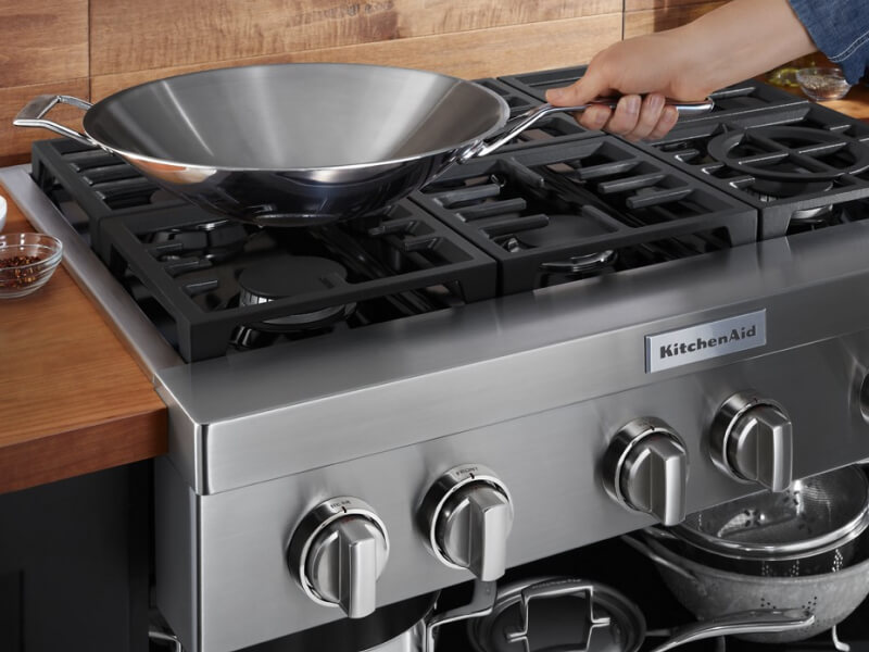 A person placing a wok on a KitchenAid® gas commercial-style cooktop