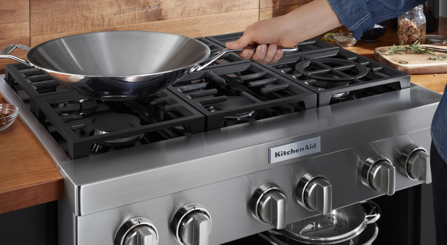 A person placing a wok on a KitchenAid® gas commercial-style cooktop