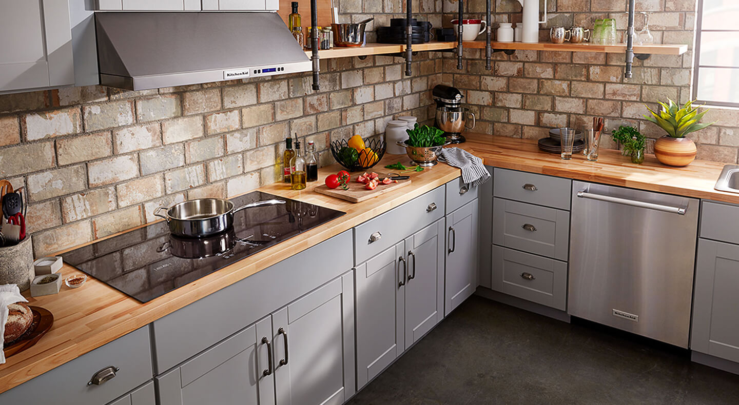 A kitchen with a glass cooktop and veggies on a cutting board nearby