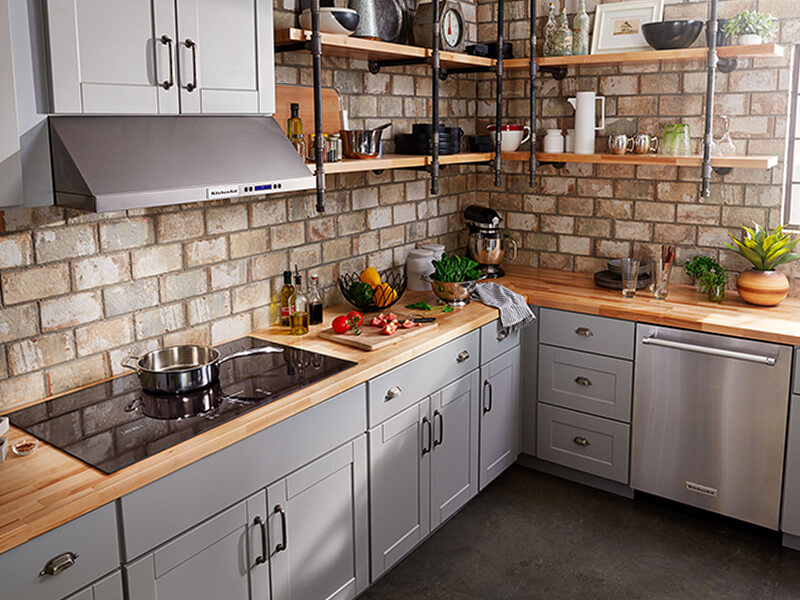 A kitchen with a glass cooktop and veggies on a cutting board nearby