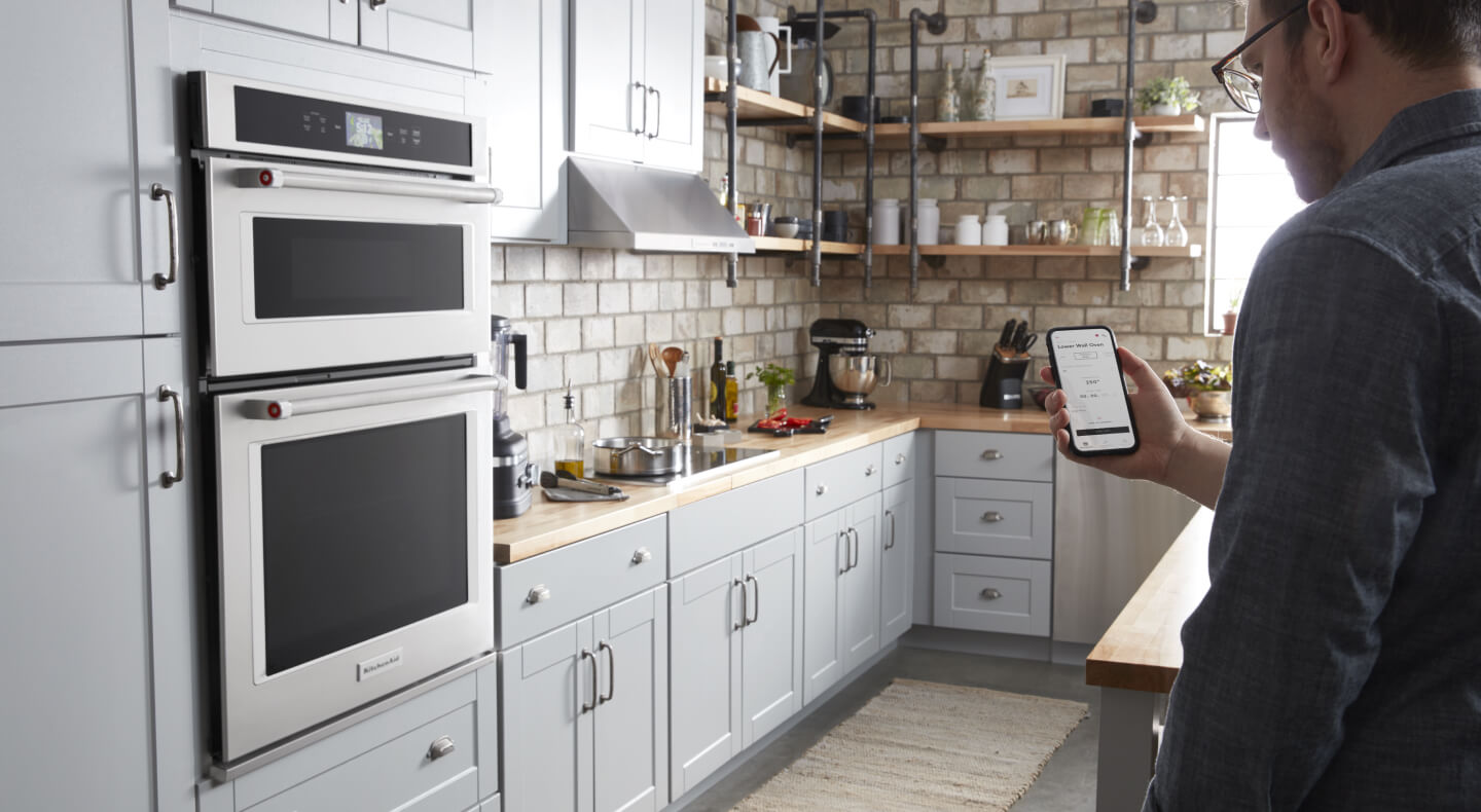 Person holding a smart phone in a bright kitchen with stainless steel appliances