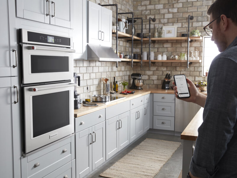 Person holding a smart phone in a bright kitchen with stainless steel appliances
