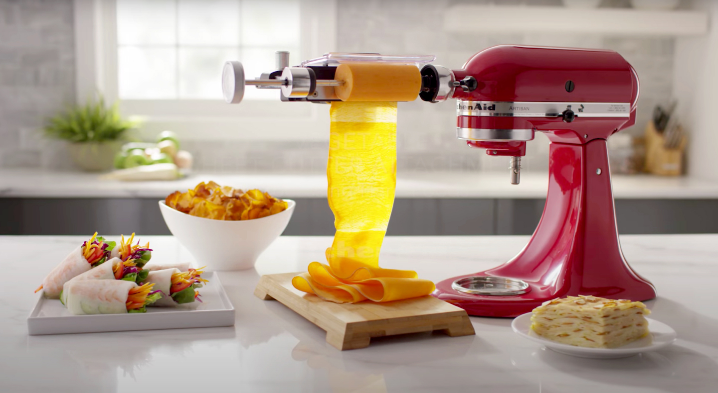 KitchenAid® stand mixer with Vegetable Sheet Cutter next to a plate of hand rolls