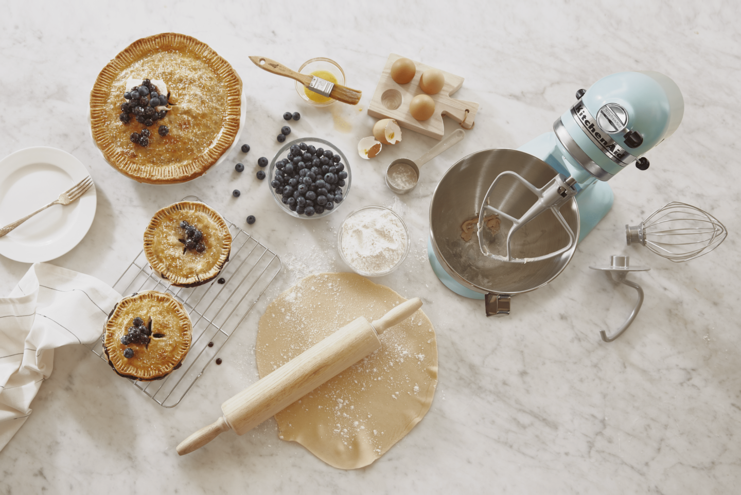 Top view of large blueberry pie and two smaller pies along with KitchenAid® stand mixer on countertop