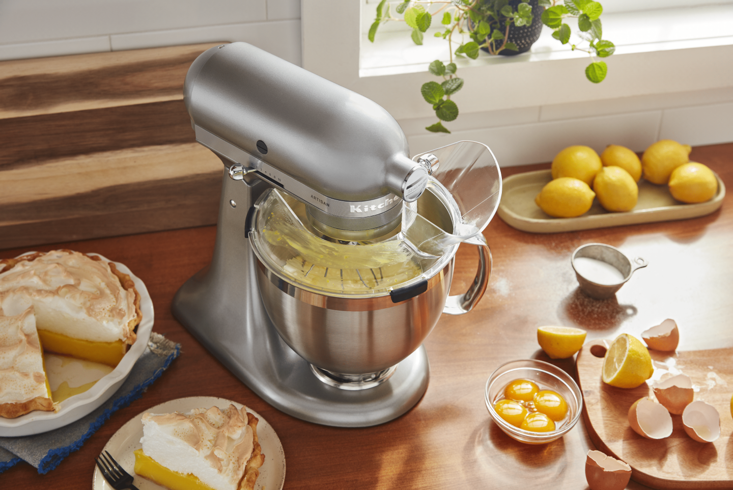 Silver KitchenAid® stand mixer with Pour Shield on countertop with lemon meringue pie and ingredients