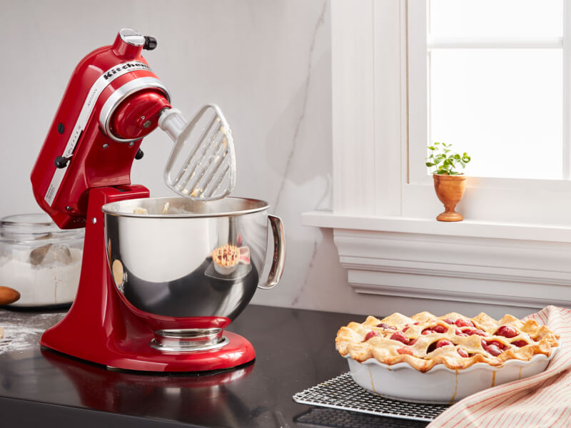A KitchenAid® stand mixer with a pastry beater accessory next to a pie on the counter of a modern kitchen.