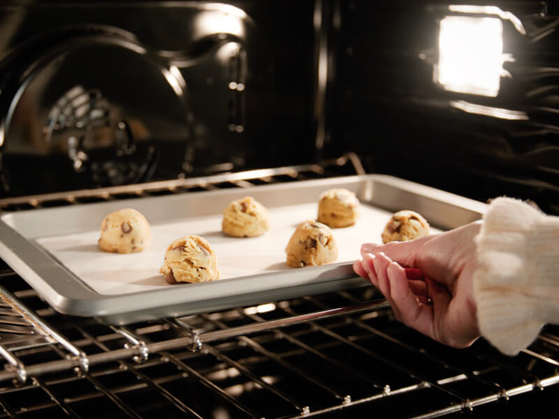 Person putting cookie dough balls in the oven