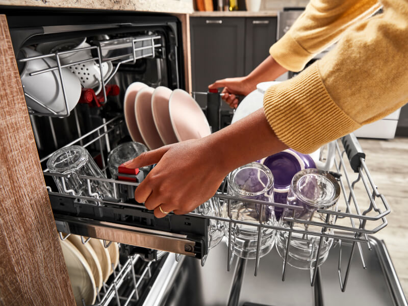 Person pulling out a dishwasher rack filled with cups and plates
