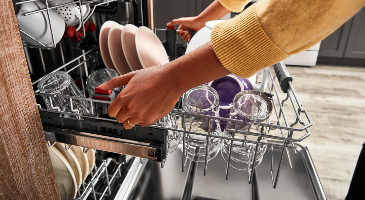 Person pulling out a dishwasher rack filled with cups and plates