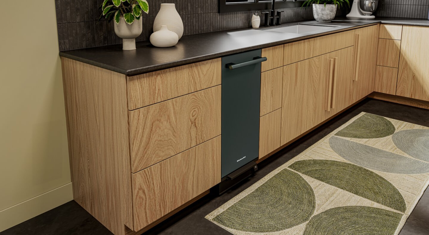 A KitchenAid® trash compactor shown in a kitchen with wooden cabinetry