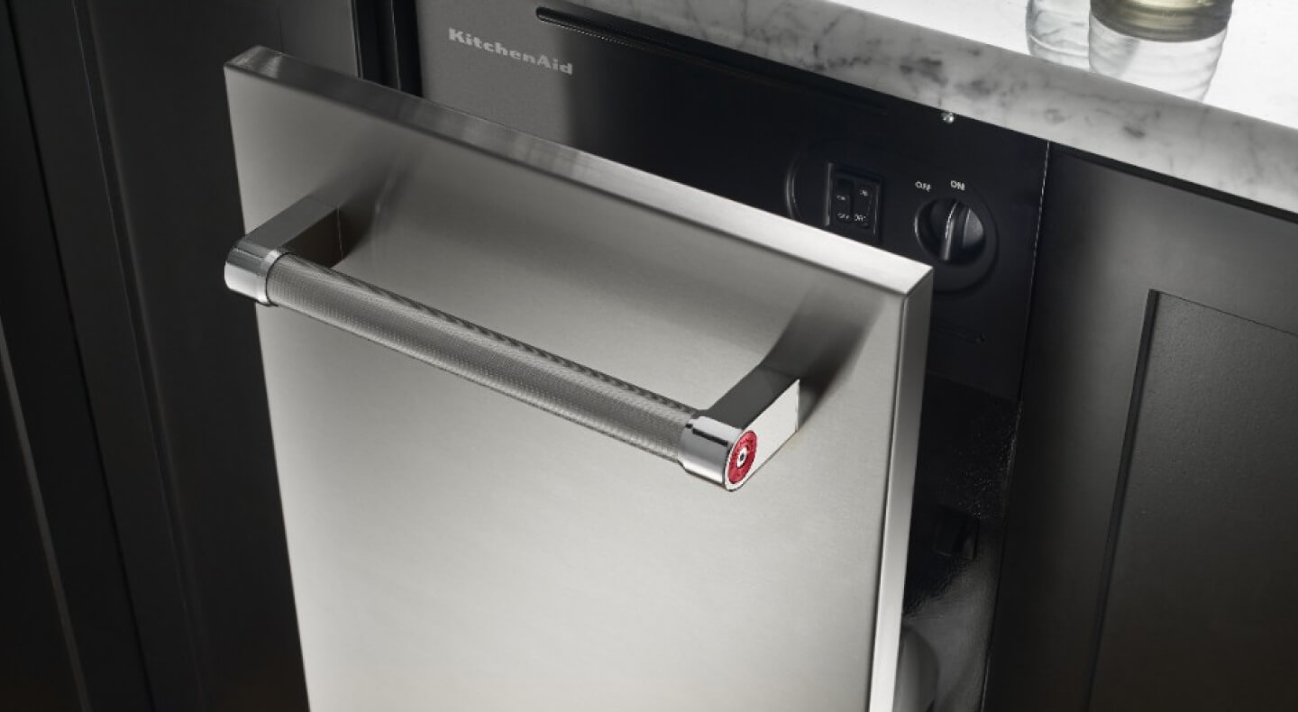 A KitchenAid® trash compactor shown slightly open in a kitchen