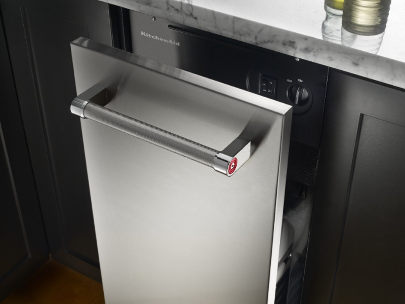 A KitchenAid® trash compactor shown slightly open in a kitchen