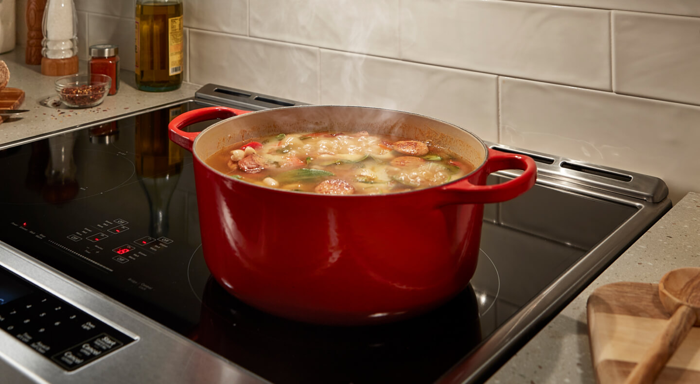 A sausage-based stew cooking in a red Dutch oven on a stovetop