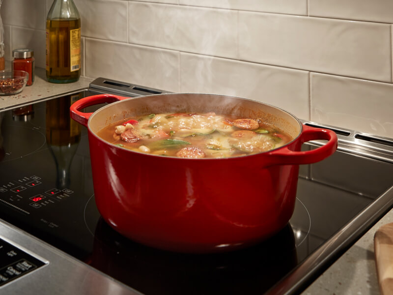 A sausage-based stew cooking in a red Dutch oven on a stovetop