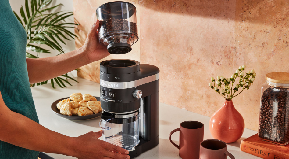 A woman using a black KitchenAid® coffee grinder to grind coffee beans