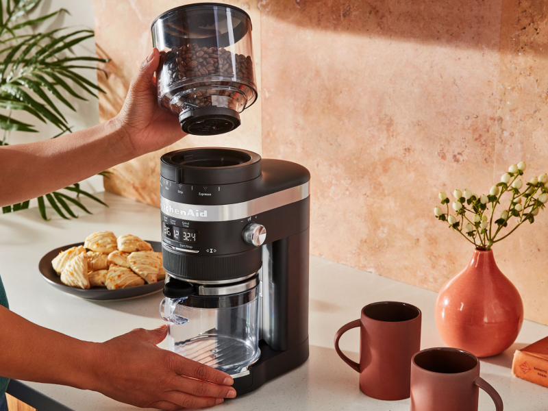 A woman using a black KitchenAid® coffee grinder to grind coffee beans