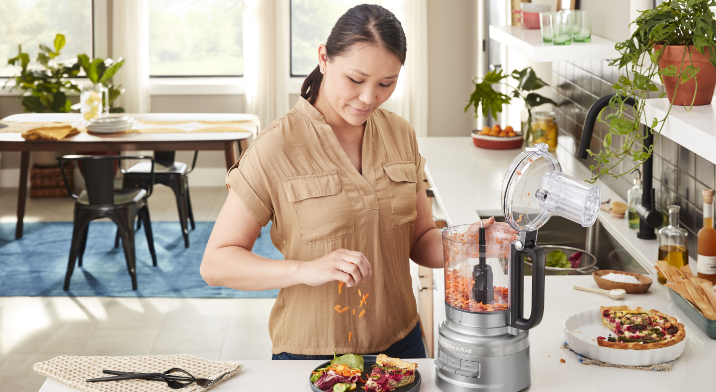 Woman placing carrots grated in KitchenAid® food processor on salad