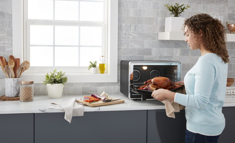 Woman removing roasted chicken from KitchenAid countertop oven 
