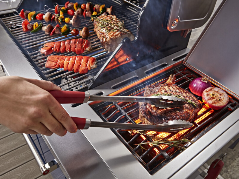 Person grilling steak and vegetables on an outdoor grill